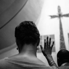 A black woman crosses her fingers in the church.